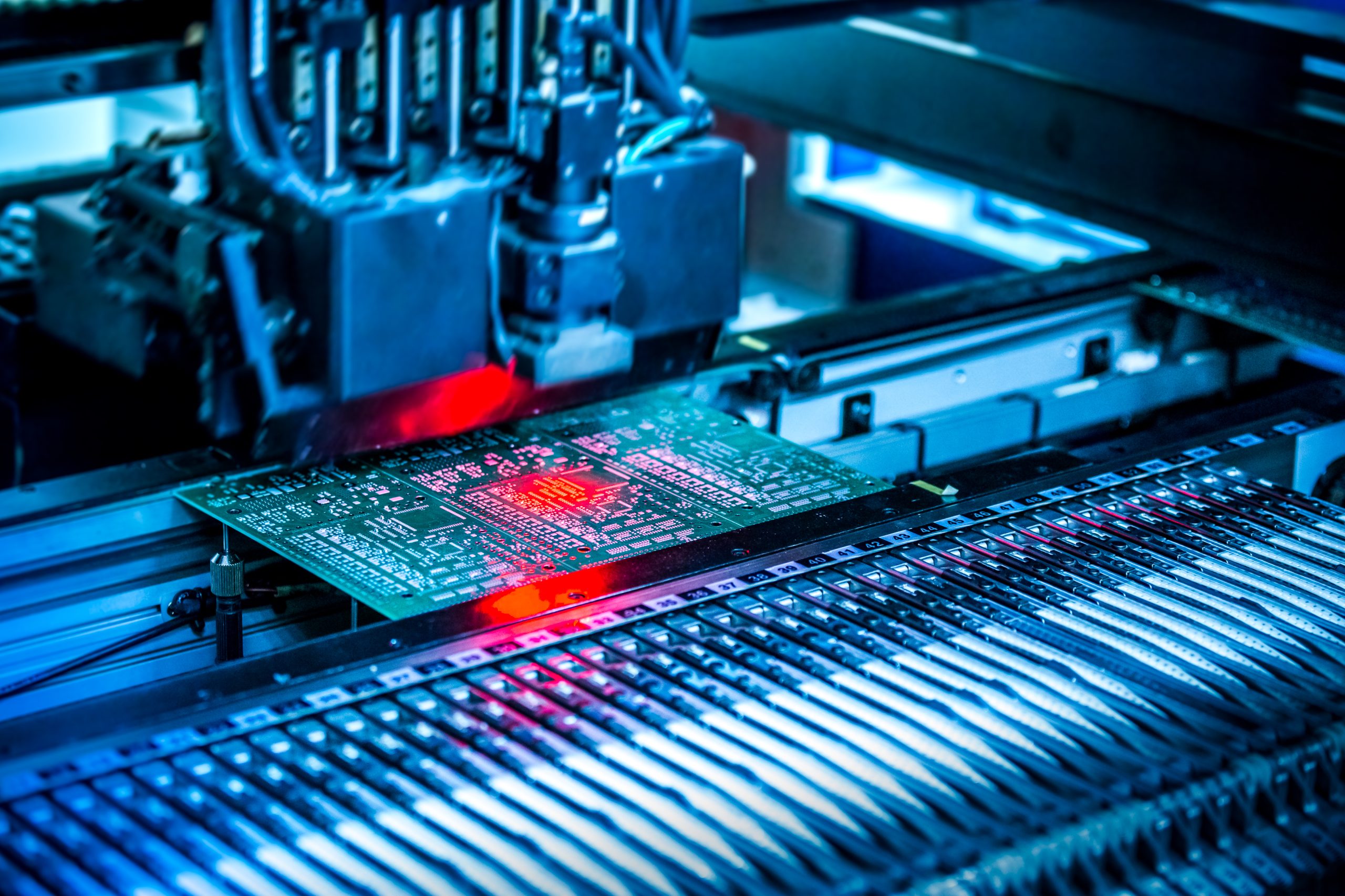 INSIGHTS Electronic circuit under surface-mounting machine. Shot in red and blue tints. Surface-mount technology as a producing of electronic circuits. Components placed onto the surface of printed elements.